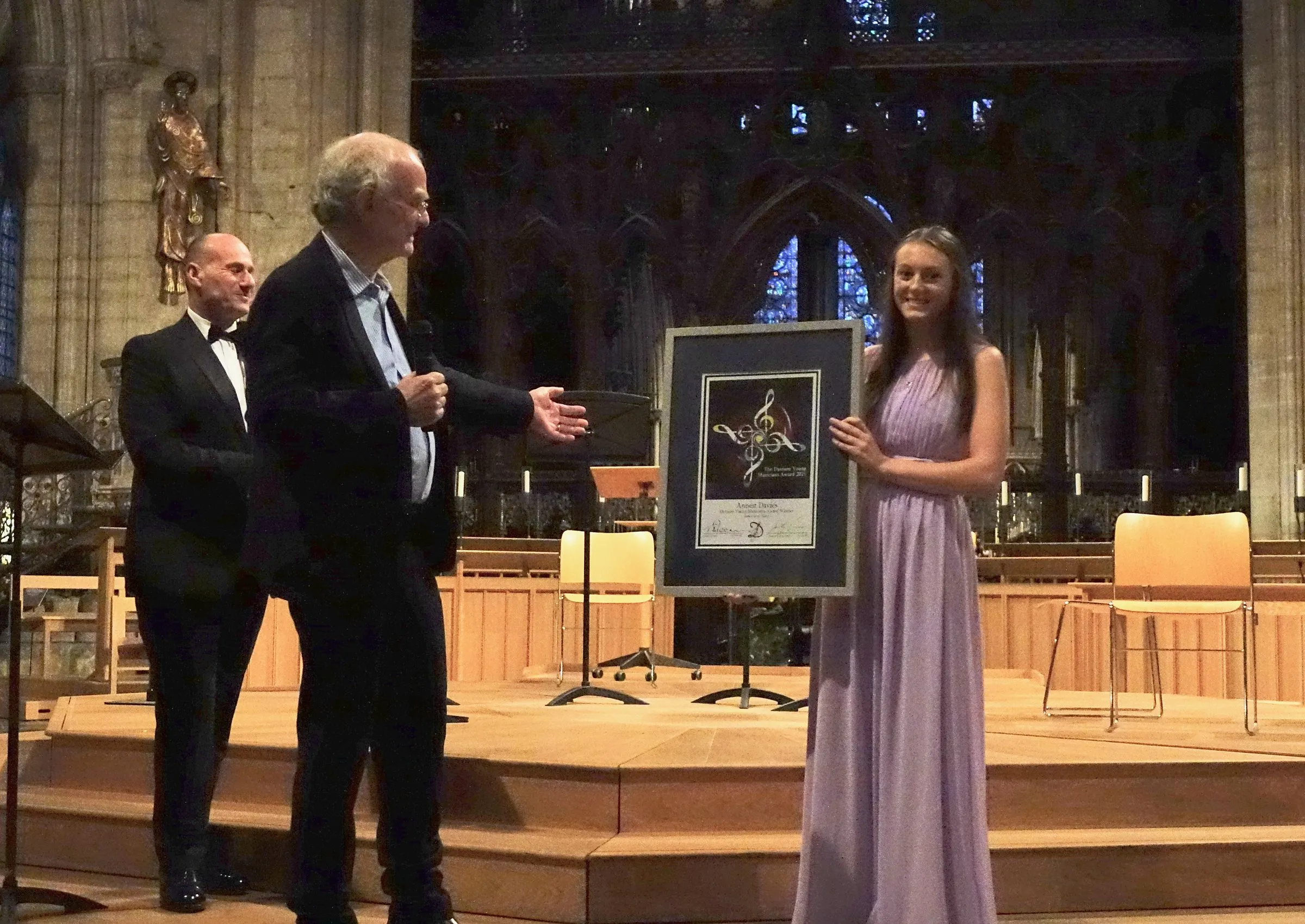 A framed award is presented to a musician on the cathedral stage