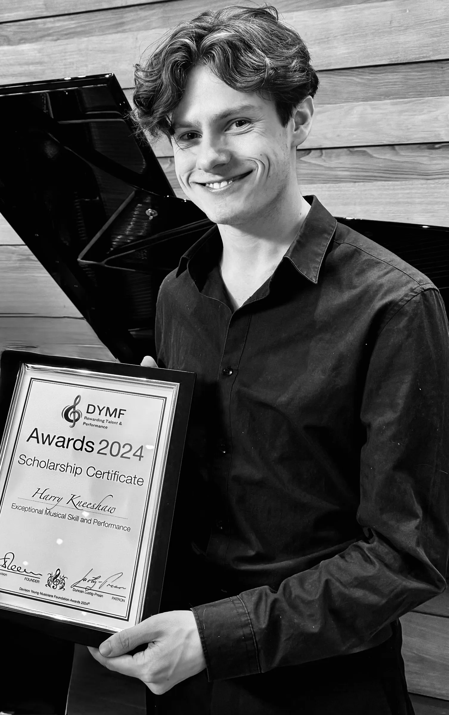 A young musician holds his framed Awards 2024 scholarship certificate, in black and white