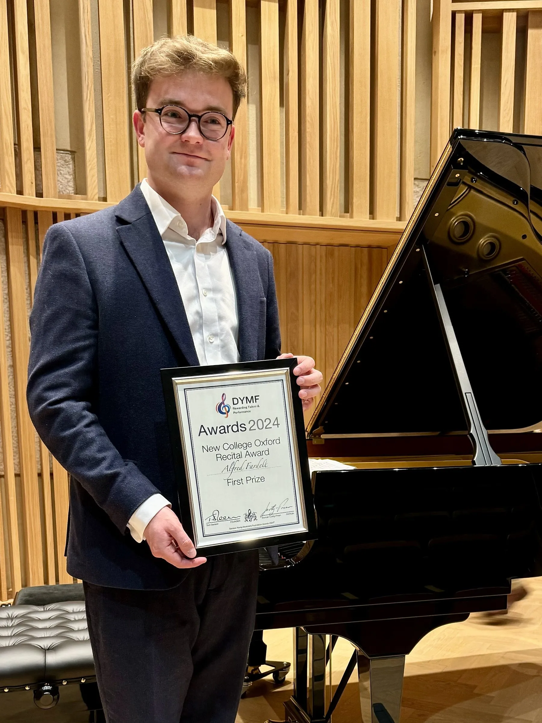 The award winner holds his framed certificate beside the piano