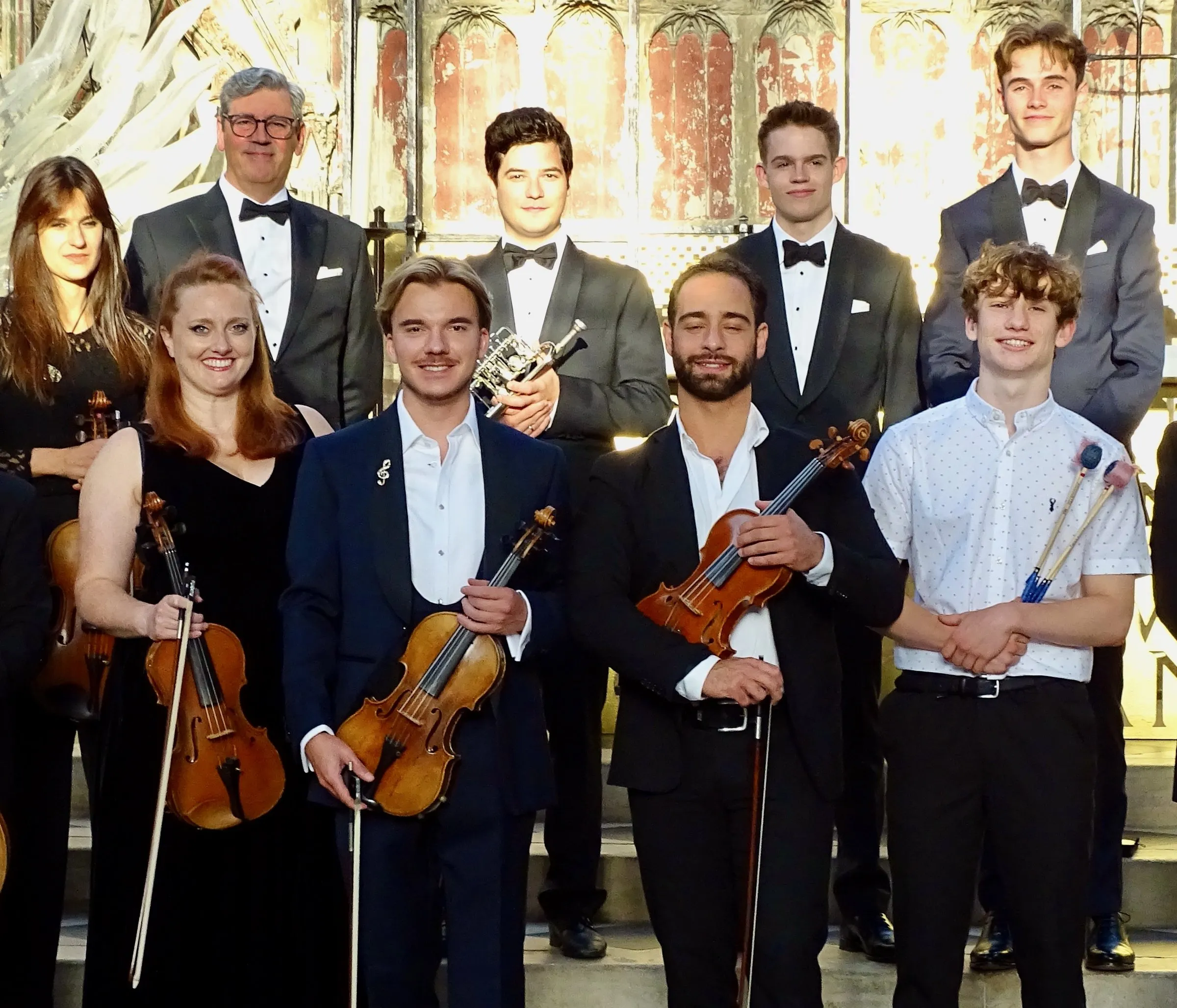 The ensemble in evening dress, with their instruments, in front of carved stone