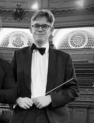 Felix Kirkby in black tie, holding a conductor's baton, in black and white
