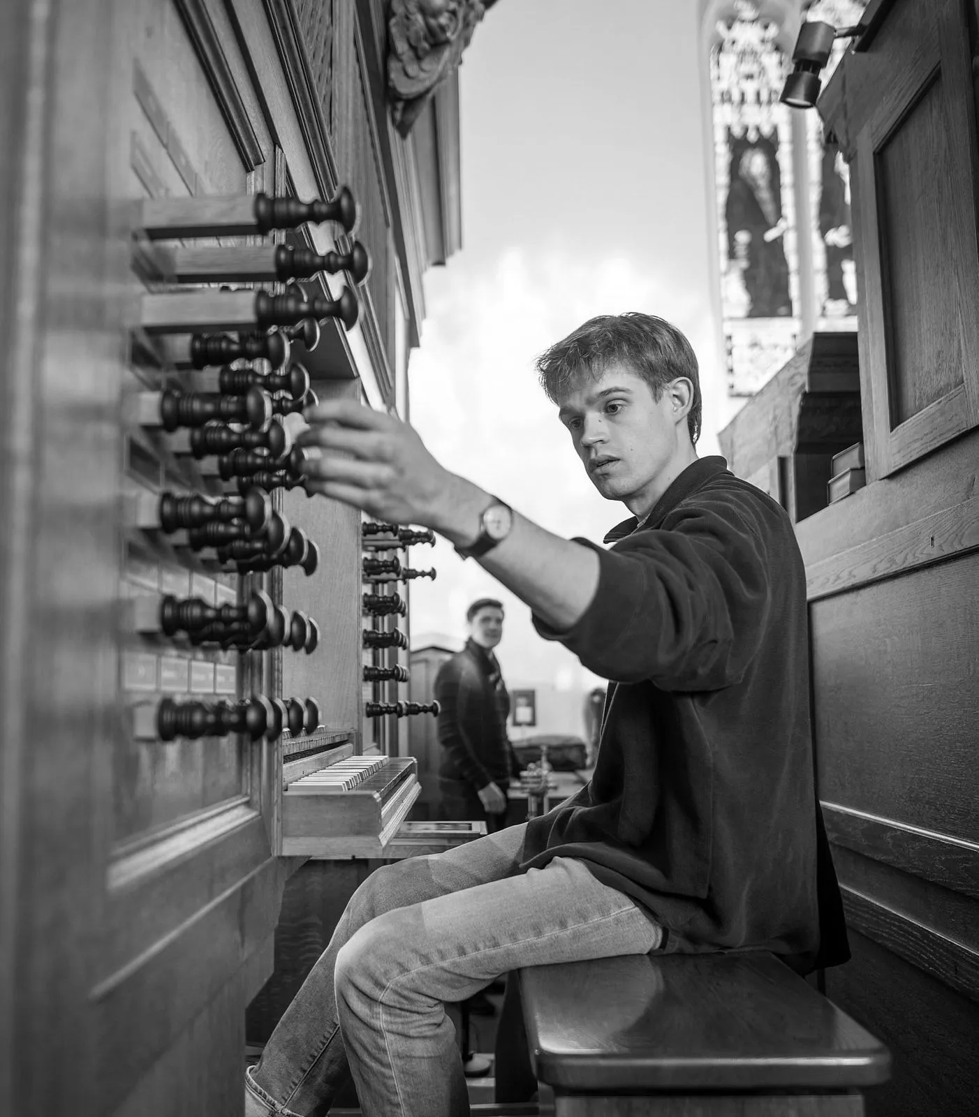Felix Kirkby seated at the organ console, reaching for a stop, in black and white