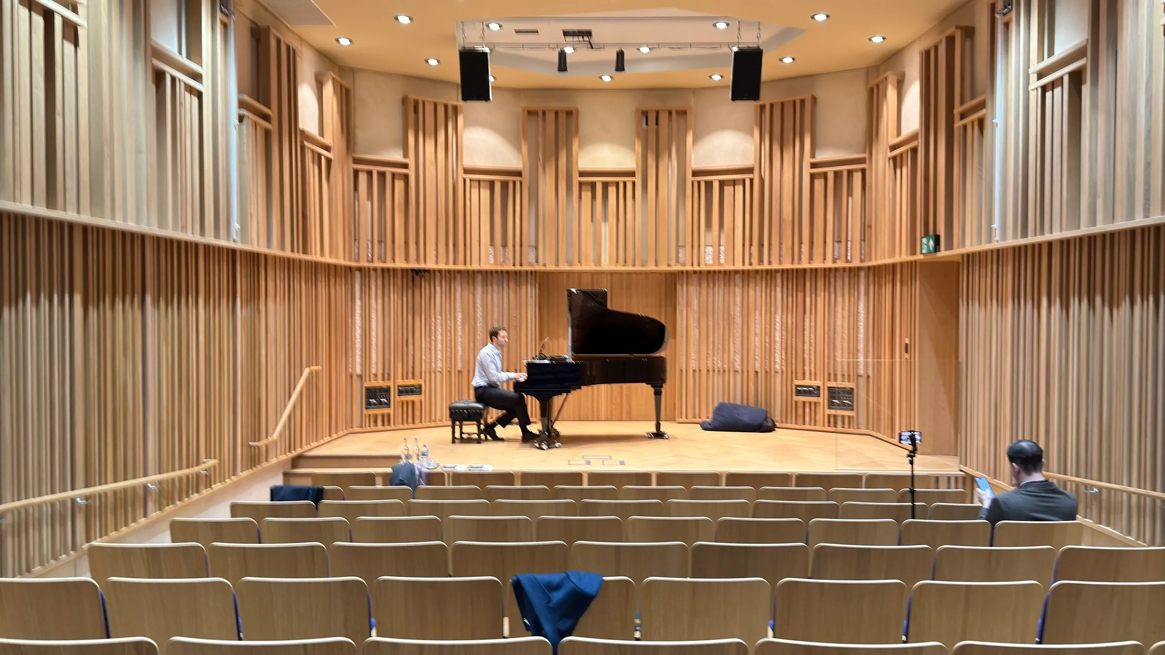 A pianist on stage in the wood-panelled New Space Recital Hall at New College, Oxford