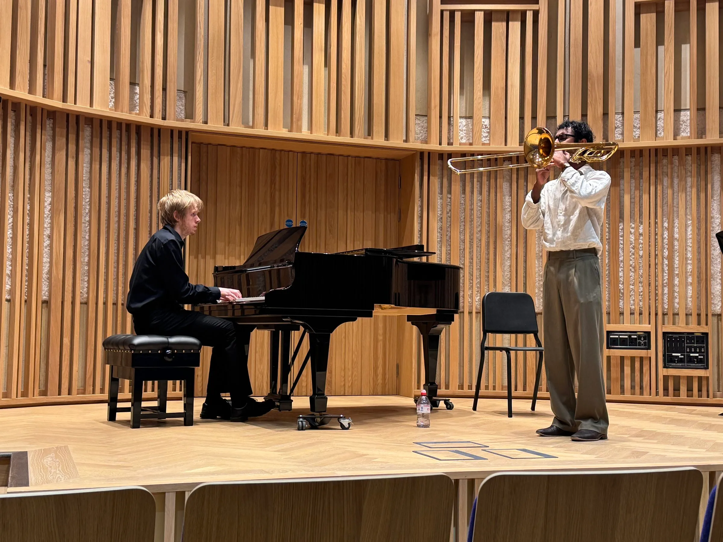 A trombonist and pianist perform on the curved wooden stage of the New Space Recital Hall, New College
