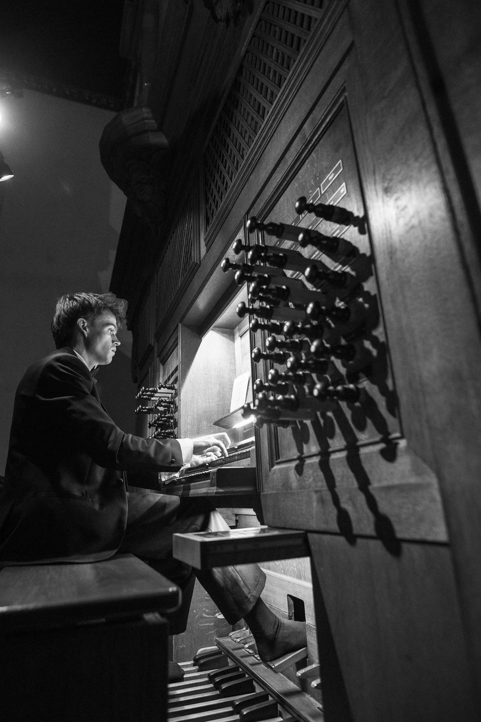 An organist at the chapel organ console, in black and white