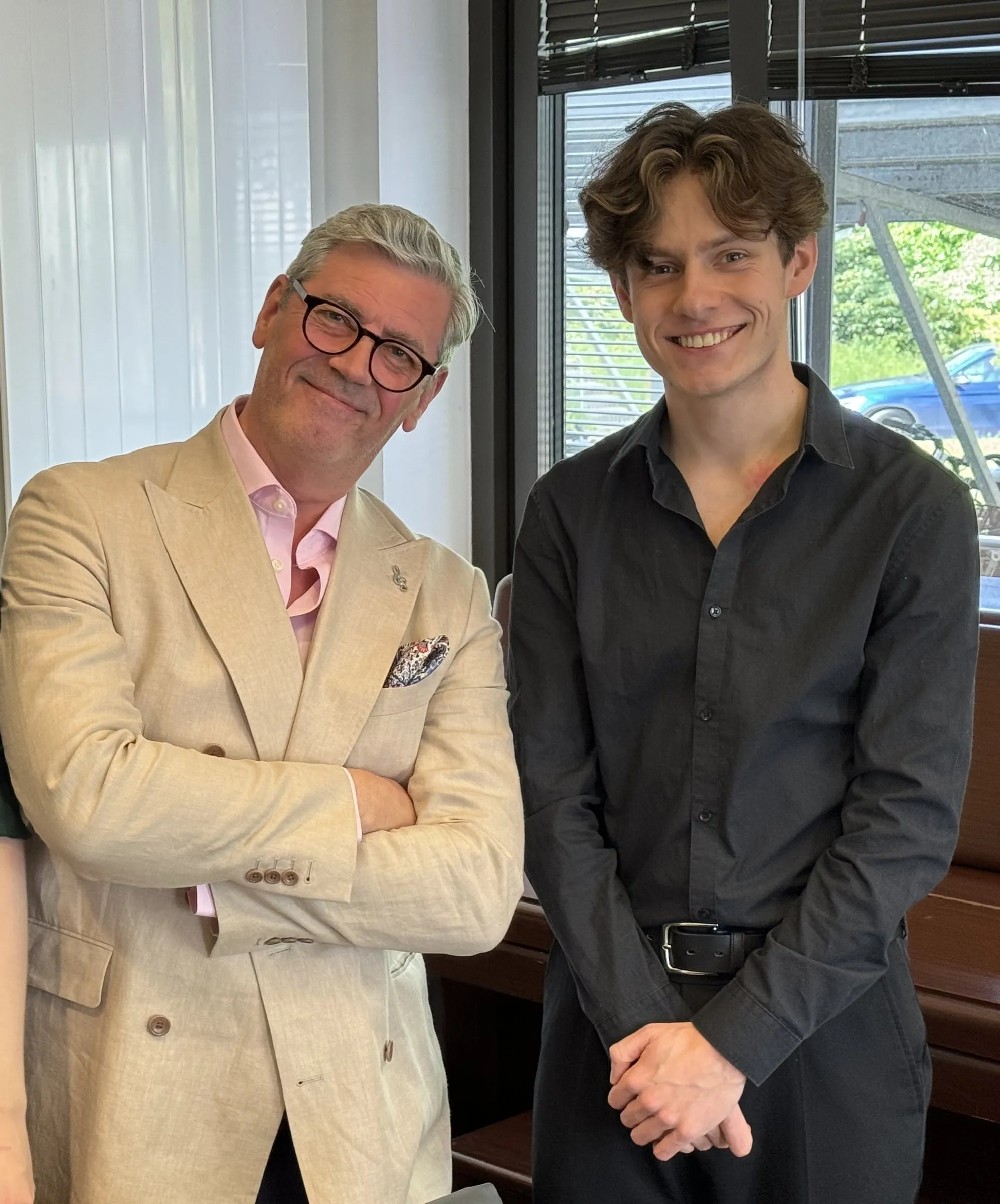A man and a young musician pose together by a window
