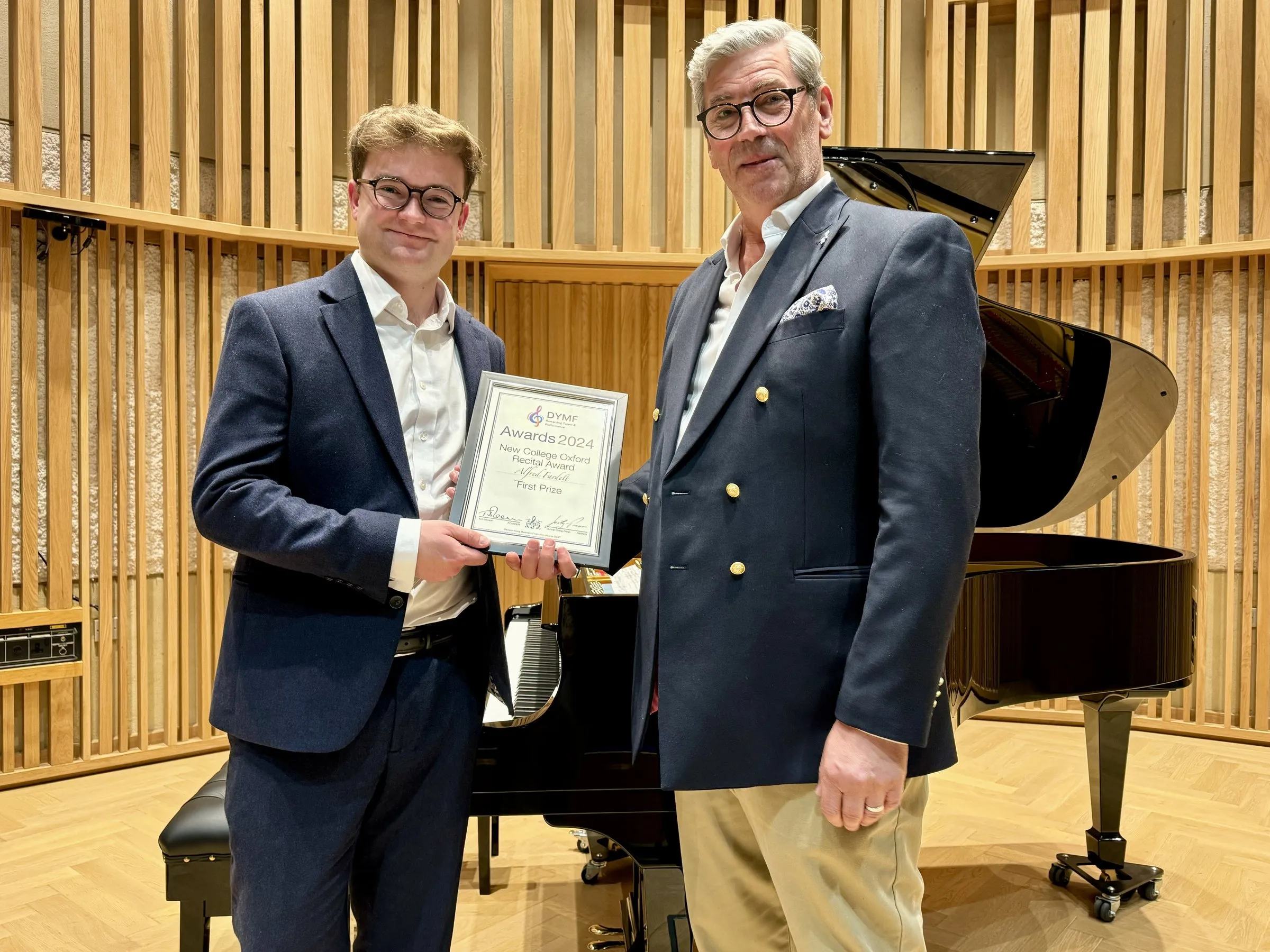 A young pianist is presented with his framed award beside the grand piano