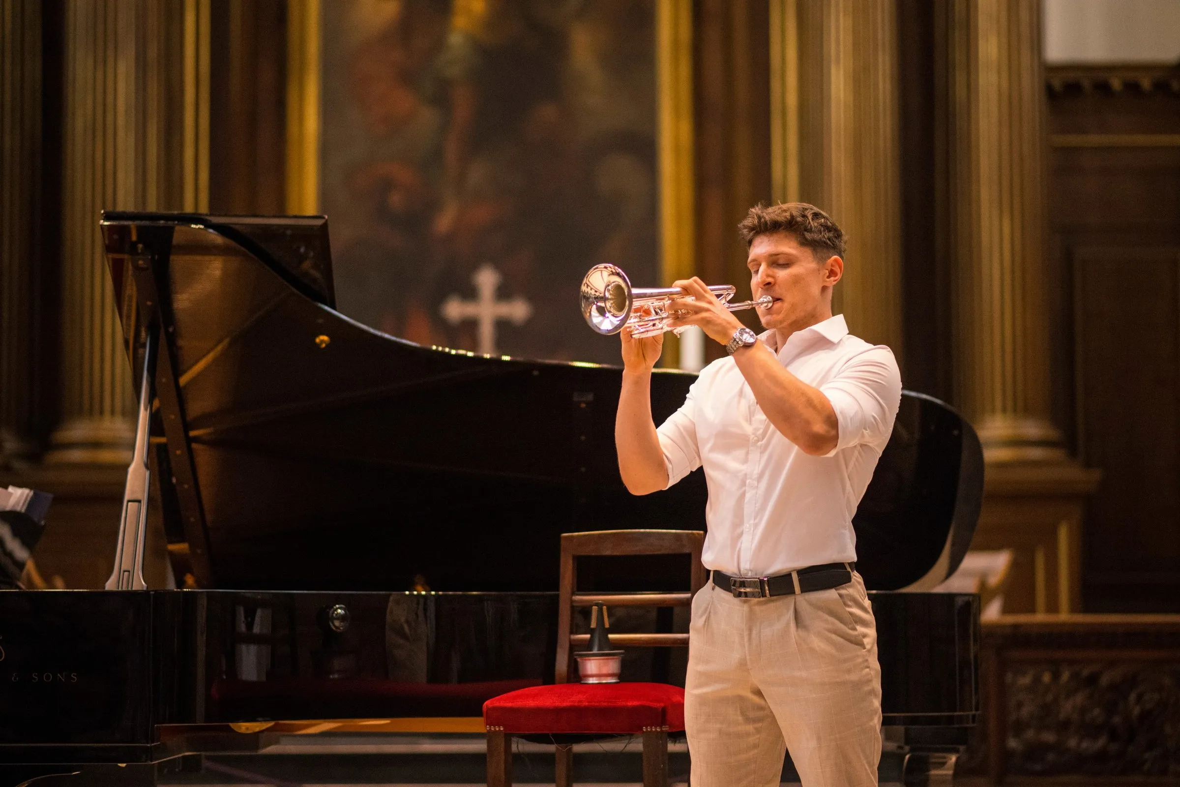 A trumpeter in a white shirt performs beside the grand piano in Trinity College Chapel