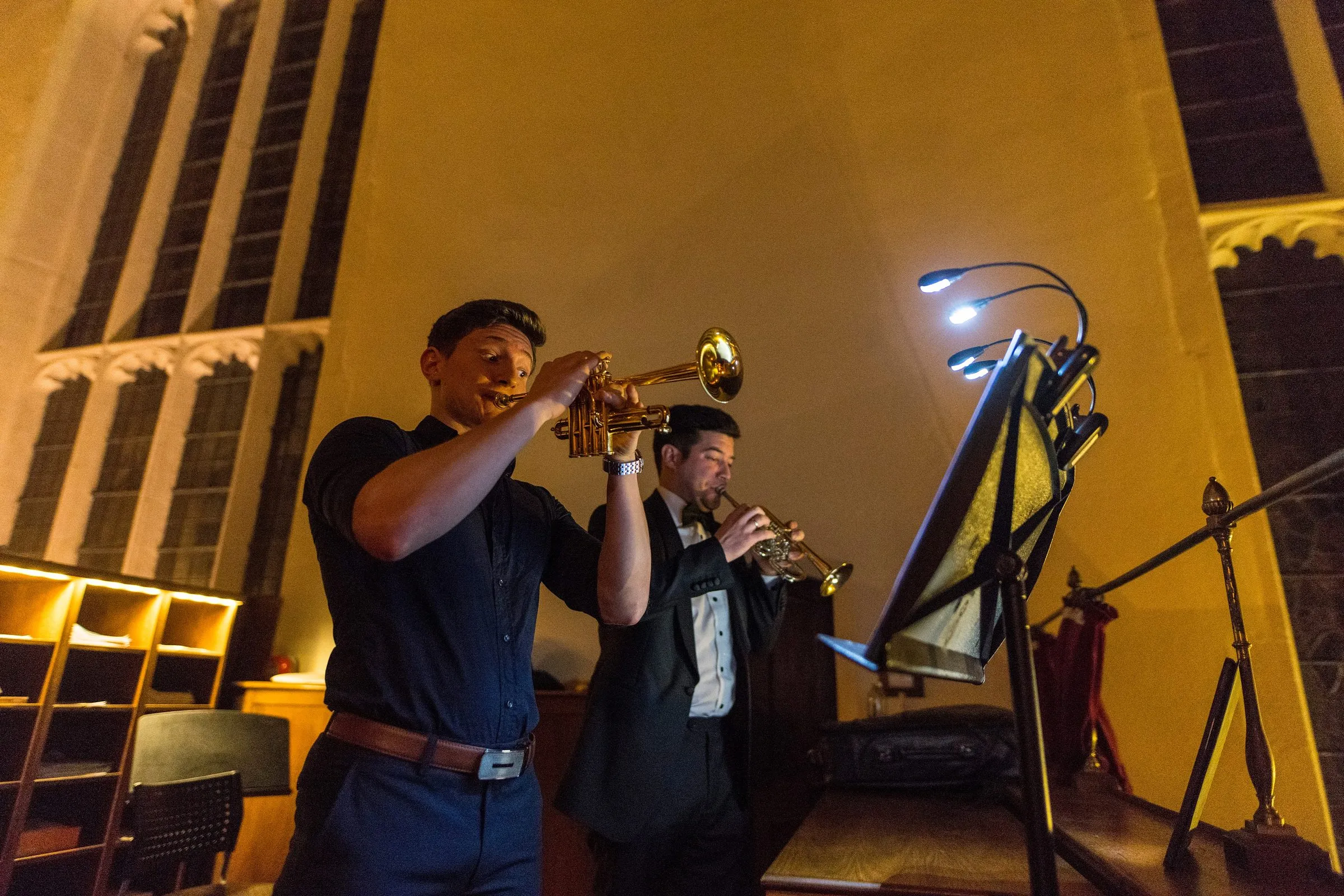 Two trumpeters play in a candlelit corner of the chapel
